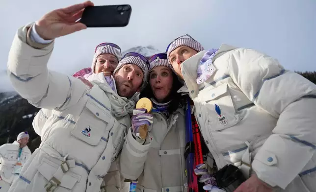 Julia Simon, of France, center, poses for a selfie with the gold medal for the women's 15-kilometer individual biathlon race at the 2026 Winter Olympics in Anterselva, Italy, Wednesday, Feb. 11, 2026. (AP Photo/Mosa'ab Elshamy)