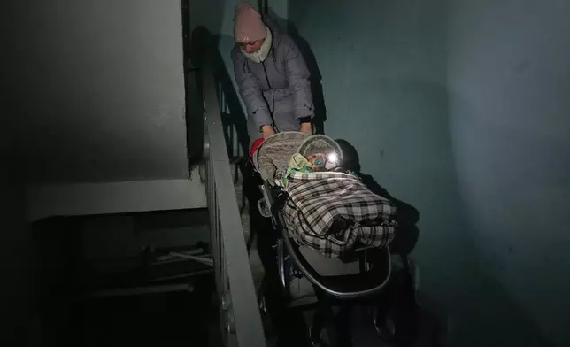 Yuliia Dolotova, 37, pulls her son in his stroller up the stairs in an apartment block during a power outage caused by Russia’s repeated air strikes on the country’s power grid, in Kyiv, Ukraine, Monday, Feb. 2, 2026. (AP Photo/Sergey Grits)