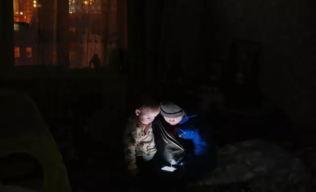 Daniil Dolotov, 11, plays on a phone with his brother Bohdanchyk, 18 months, in their apartment during a power outage caused by Russia’s repeated air strikes on the country’s power grid, in Kyiv, Ukraine, Monday, Feb. 2, 2026. (AP Photo/Sergey Grits)
