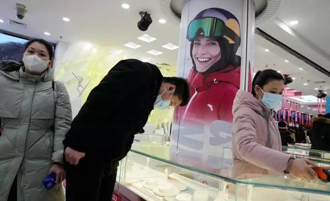 FILE - Shoppers look at official Olympics merchandise near a photo showing Chinese gold medalist Eileen Gu as the 2022 Winter Olympics nears its end, Feb. 19, 2022, in Beijing. (AP Photo/Ng Han Guan, File)
