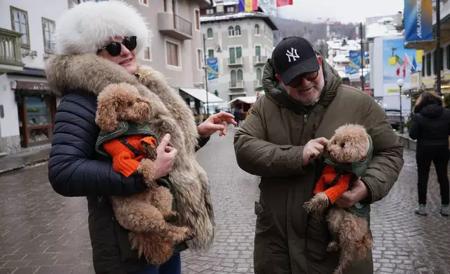 Husband and wife, Christina and Roberto, pose for a photo with their poodles, Gualtiero, left, and Leone, wearing customised Loro Piana jackets, in Cortina d'Ampezzo, Italy, on Saturday, Feb. 14, 2026. (AP Photo/Alessandra Tarantino)