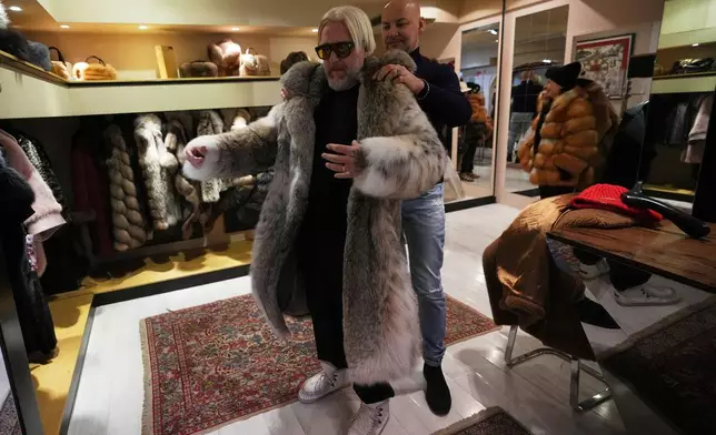 Sales manager for Pajaro, a luxury Italian fashion brand, Marco Molinari, right, helps his client, Stefano Vannicola, put on a fur coat in Cortina d'Ampezzo, Italy, Saturday, Feb. 14, 2026. (AP Photo/Alessandra Tarantino)