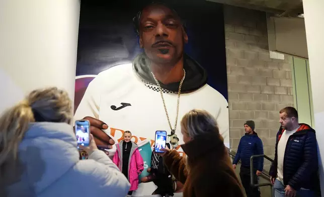 Fans pose for a photograph in front of a mural of Swansea City minority co-owner Snoop Dogg ahead of the English Championship soccer match between Swansea City and Preston in Swansea, Wales, Tuesday, Feb. 24, 2026. (Jacob King/PA via AP)