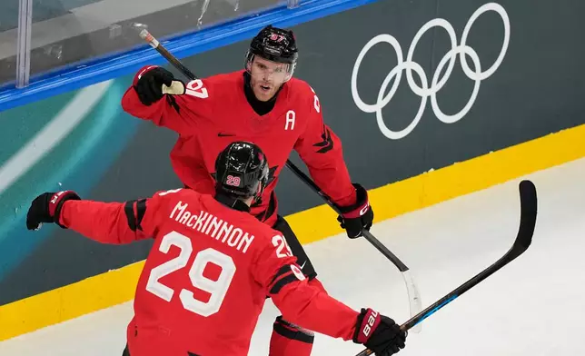 Canada's Connor McDavid, back, celebrates with Canada's Nathan MacKinnon after scoring his sides first goal during a preliminary round match of men's ice hockey between Canada and Switzerland at the 2026 Winter Olympics, in Milan, Italy, Friday, Feb. 13, 2026. (AP Photo/Hassan Ammar)