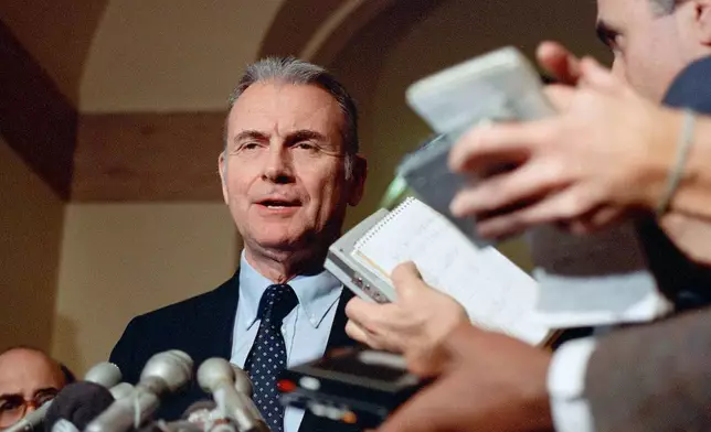 FILE - Reporters hold up tape recorders as Rep. Lee Hamilton, D-Ind., makes comments on Capitol Hill, in Washington, Dec. 18, 1986. (AP Photo/Dennis Cook, File)