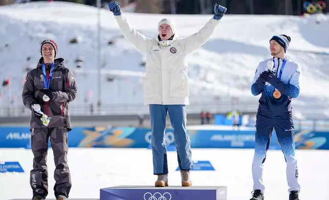 Gold medalist Jens Luraas Oftebro, of Norway, celebrates on the podium flanked by silver medalist Johannes Lamparter, of Austria, left, and bronze medalist Ilkka Herola, of Finland, after the nordic combined individual Gundersen large hill/10km at the 2026 Winter Olympics, in Tesero, Italy, Tuesday, Feb. 17, 2026. (AP Photo/Matthias Schrader)