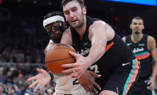 Phoenix Suns guard Jordan Goodwin, left, and San Antonio Spurs center Luke Kornet, right, scramble for a loose ball during the first half of an NBA basketball game in Austin, Texas, Thursday, Feb. 19, 2026. (AP Photo/Eric Gay)