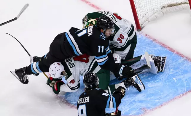 Utah Mammoth right wing Dylan Guenther (11) is knocked down in front of the net by Minnesota Wild defenseman Jared Spurgeon, bottom center, during the first period of an NHL hockey game, Friday, Feb. 27, 2026, in Salt Lake City. (AP Photo/Tyler Tate)