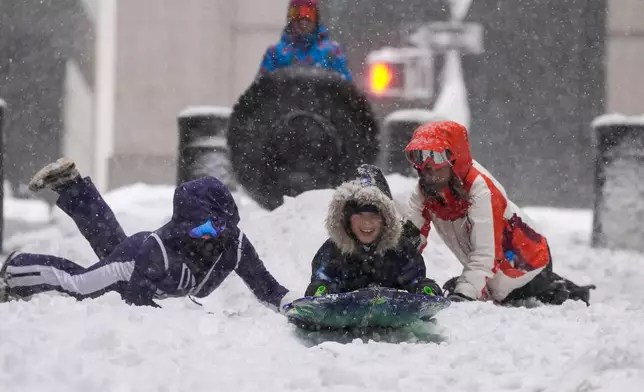 Jack Wilson, center, sleds down a street in lower Manhattan during a snow storm, Monday, Feb. 23, 2026, in New York. (AP Photo/Seth Wenig)