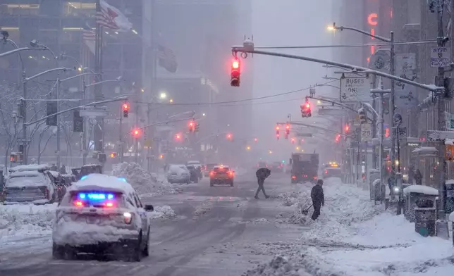A law enforcement vehicle makes its way down Sixth Avenue as pedestrians cross during a snow storm, Monday, Feb. 23, 2026, in New York. (AP Photo/Seth Wenig)