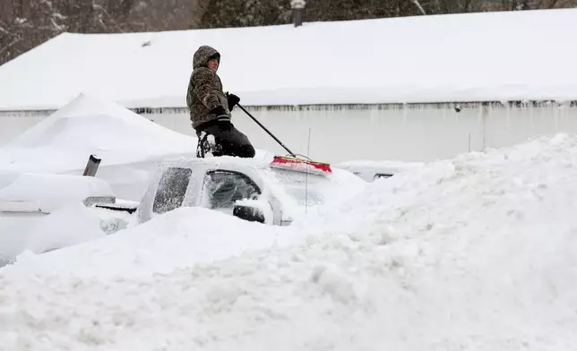 A man clears snow off of cars and trucks in a contractor's parking lot, Monday, Feb. 23, 2026, in St. James, N.Y. (AP Photo/Heather Khalifa)