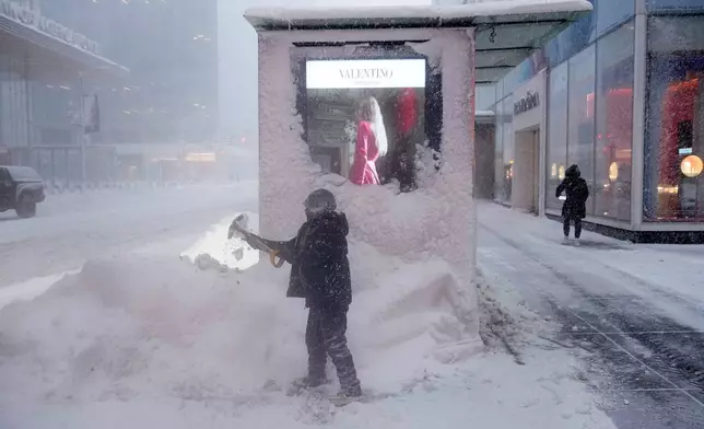 A man shovels snow around a bus stop during a snow storm, Monday, Feb. 23, 2026, in New York. (AP Photo/Seth Wenig)