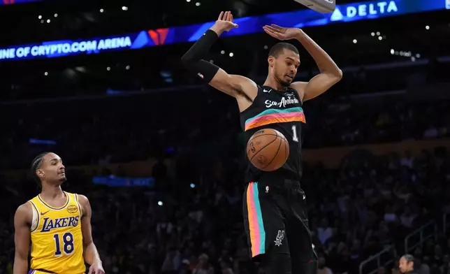 San Antonio Spurs forward Victor Wembanyama (1) descends after making a dunk as Los Angeles Lakers guard Kobe Bufkin (18) looks on during the first half of an NBA basketball game Tuesday, Feb. 10, 2026, in Los Angeles. (AP Photo/Jae C. Hong)