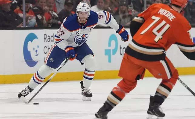Edmonton Oilers center Connor McDavid, left, looks to pass as Anaheim Ducks defenseman Ian Moore defends during the second period of an NHL hockey game Wednesday, Feb. 25, 2026, in Anaheim, Calif. (AP Photo/Gregory Bull)