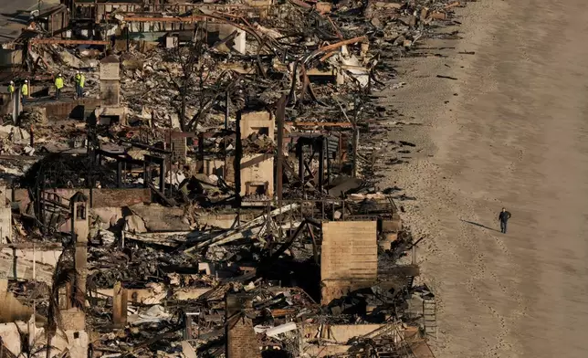FILE - A person walks on the beach next to homes damaged by the Palisades Fire, Jan. 16, 2025, in Malibu, Calif. (AP Photo/Jae C. Hong, File)