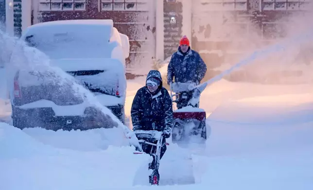 Neighbors team up to clear a driveway, Monday, Feb. 23, 2026, in North Attleborough, Mass. Over two feet of snow fell on the area after a blizzard passed through. (AP Photo/Mark Stockwell)