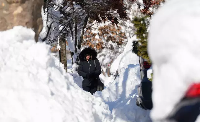 A woman navigates around piles of shoveled snow as she makes her way down a sidewalk, Tuesday, Feb. 24, 2026, in Weekhawken, N.J. (AP Photo/Seth Wenig)