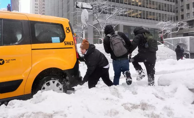 Cameron Betz helps push a taxi stuck in the snow during a snow storm, Monday, Feb. 23, 2026, in New York. (AP Photo/Seth Wenig)