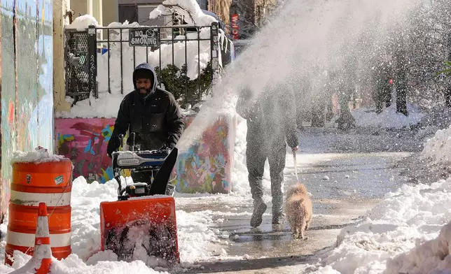 A worker uses a snow blower to clear snow from a sidewalk in front of retail shops, Tuesday, Feb. 24, 2026, in the Brooklyn borough of New York. (AP Photo/Yuki Iwamura)