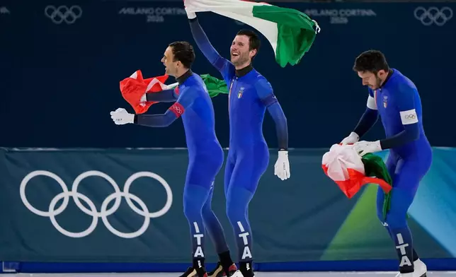 Team Italy with Davide Ghiotto, white armband, Andrea Giovannini, red armband, and Michele Malfatti, blue armband, celebrate winning the gold medal in the final of the men's team pursuit speedskating race at the 2026 Winter Olympics, in Milan, Italy, Tuesday, Feb. 17, 2026. (AP Photo/Ben Curtis)