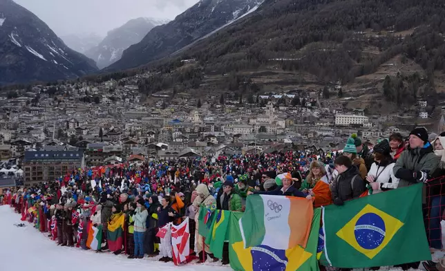 Spectators hold flags, including the Brazilian flag, right, as they watch an alpine ski, men's giant slalom race, at the 2026 Winter Olympics, in Bormio, Italy, Saturday, Feb. 14, 2026. (AP Photo/Julia Demaree Nikhinson)