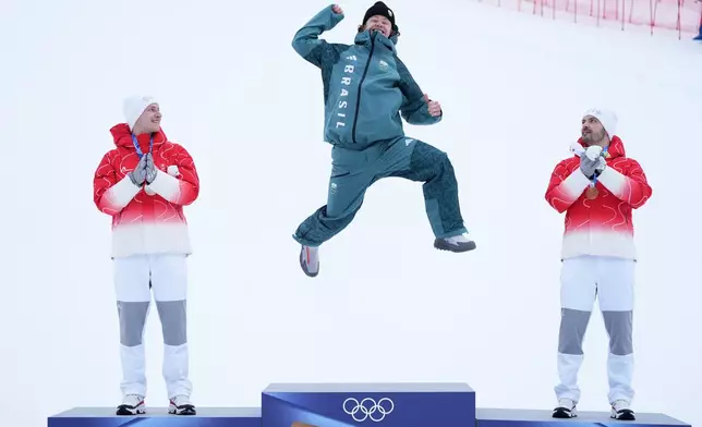 Brazil's Lucas Pinheiro Braathen, center, celebrates winning a gold medal for an alpine ski, men's giant slalom race, as silver medalist Switzerland's Marco Odermatt, right, and bronze medalist Switzerland's Loic Meillard applaud, at the 2026 Winter Olympics, in Bormio, Italy, Saturday, Feb. 14, 2026. (AP Photo/Rebecca Blackwell)