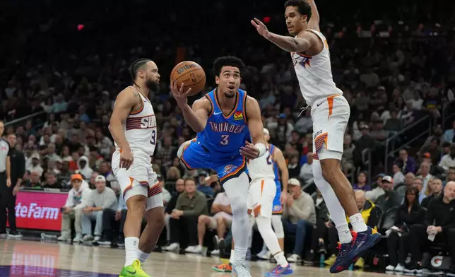 Oklahoma City Thunder guard Jared McCain scores between Phoenix Suns forward Dillon Brooks (3) and forward Oso Ighodaro during the first half of an NBA basketball game, Wednesday, Feb. 11, 2026, in Phoenix. (AP Photo/Rick Scuteri)
