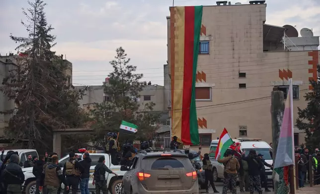 Kurdish-led Syrian Democratic Forces (SDF) combatants, right, hold a Kurdish flag as they watch a convoy of Syria's Interior Ministry security forces deployed under an agreement aimed at stabilizing a ceasefire, in Qamishli, eastern Syria, Tuesday, Feb. 3, 2026. (AP Photo/Baderkhan Ahmad)