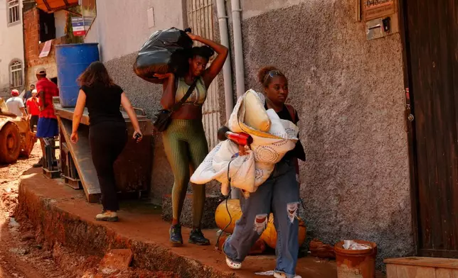 Residents carry away their belongings at the site where homes collapsed due to heavy rains and flooding in the Parque Burnier neighborhood of Juiz de Fora, Minas Gerais state, Brazil, Wednesday, Feb. 25, 2026. (AP Photo/Silvia Izquierdo)