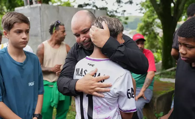 Ricardo Dutra, the father of 11-year-old Bernardo Lopes, a victim of heavy rains and flooding, is comforted by his son's friends during the funeral and burial of his child in Juiz de Fora, Minas Gerais state, Brazil Wednesday, Feb. 25, 2026. (AP Photo/Silvia Izquierdo)