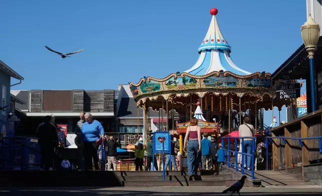 People walk in front of the carousel at Pier 39 in San Francisco, Tuesday, Oct. 21, 2025. (AP Photo/Jeff Chiu)