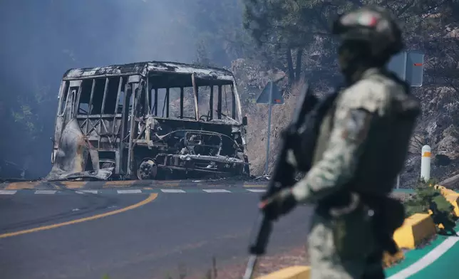 A soldier stands guard by a charred vehicle after it was set on fire, in Cointzio, Michoacán state, Mexico, Sunday, Feb. 22, 2026, following the death of the leader of the Jalisco New Generation Cartel, Nemesio Oseguera, known as "El Mencho." (AP Photo/Armando Solis)