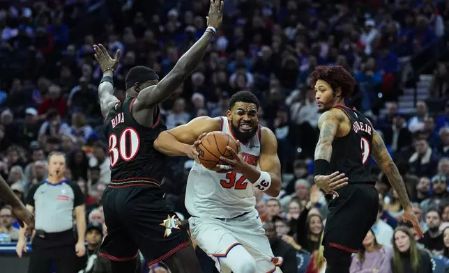 New York Knicks' Karl-Anthony Towns, center, tries to get a shot past Philadelphia 76ers' Adem Bona (30) and Kelly Oubre Jr. during the first half of an NBA basketball game, Wednesday, Feb. 11, 2026, in Philadelphia. (AP Photo/Matt Rourke)