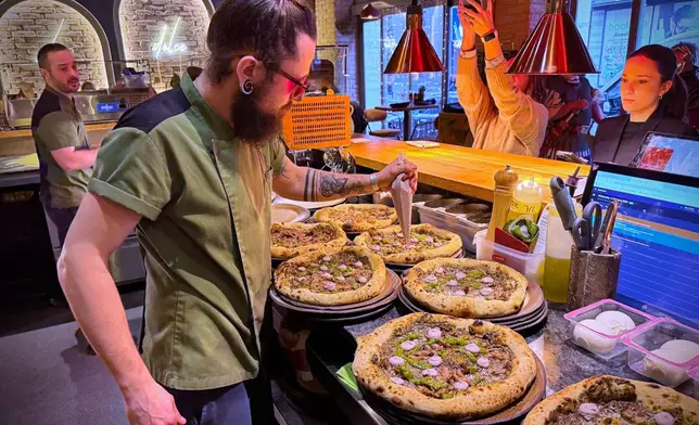Laszlo Bardossy, head chef of the Neverland Pizzeria adds topping on the restaurant's Roman-era pizza in Budapest, Hungary, on Feb. 11, 2026. (AP Photo/Bela Szandelszky)
