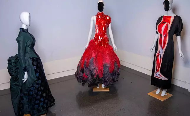 A vintage walking dress, from left, an Alexander McQueen dress, and a Christopher Kane dress are held in preparation for The Metropolitan Museum of Art's spring exhibition, "Costume Art," on Thursday, Feb. 12, 2026, in New York. (Photo by Charles Sykes/Invision/AP)
