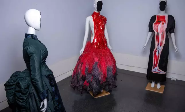 A vintage walking dress, from left, an Alexander McQueen dress, and a Christopher Kane dress are held in preparation for The Metropolitan Museum of Art's spring exhibition, "Costume Art," on Thursday, Feb. 12, 2026, in New York. (Photo by Charles Sykes/Invision/AP)