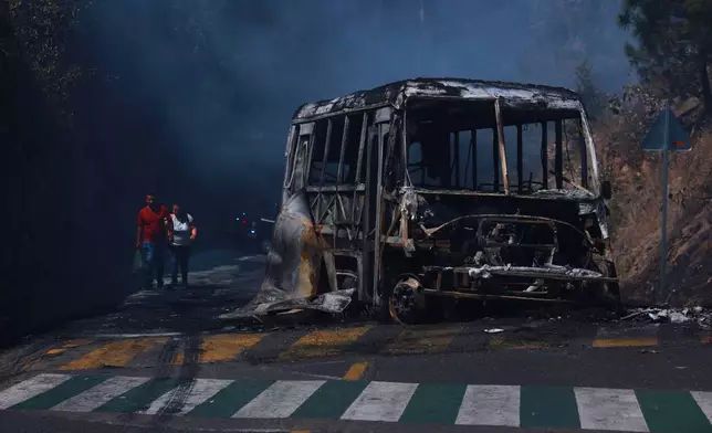 Pedestrians walk past a charred vehicle after it was set on fire, on a road in Cointzio, Michoacán state, Mexico, Sunday, Feb. 22, 2026, after the death of the leader of the Jalisco New Generation Cartel, Nemesio Rubén Oseguera Cervantes, known as "El Mencho." (AP Photo/Armando Solis)