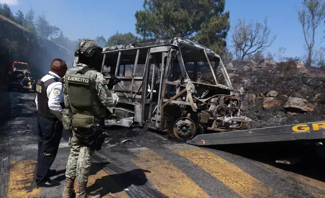 A soldier stands guard by a charred vehicle that was set on fire in Cointzio, Mexico, Sunday, Feb. 22, 2026, amid reports the Mexican Army killed Jalisco New Generation Cartel leader Nemesio Oseguera, known as "El Mencho." (AP Photo/Armando Solis)