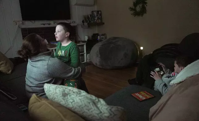 Ronan Murphy snuggles with his mom, Andrea, while looking at the snow falling outside his home while brother, Connor sits nearby in Ayer, Mass., on Saturday, Jan. 17, 2026. (AP Photo/Shelby Lum)