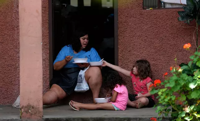 A family eats donated food at a shelter near the site where homes collapsed due to heavy rains and flooding in the Parque Burnier neighborhood of Juiz de Fora, Minas Gerais state, Brazil, Wednesday, Feb. 25, 2026. (AP Photo/Silvia Izquierdo)
