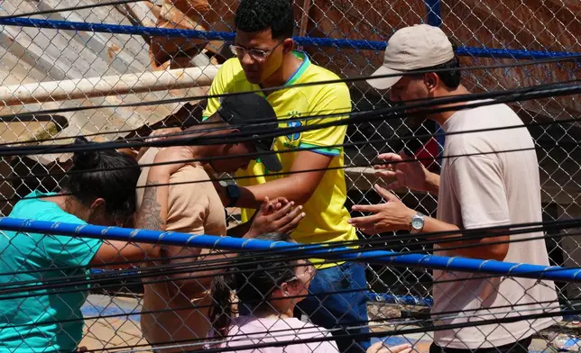 Residents pray near the site where homes collapsed due to heavy rains and flooding in the Parque Burnier neighborhood of Juiz de Fora, Minas Gerais state, Brazil, Wednesday, Feb. 25, 2026. (AP Photo/Silvia Izquierdo)
