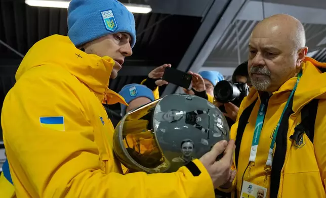Ukrainian skeleton athlete Vladyslav Heraskevych left, holds his crash helmet at the mixed zone of the sliding center at the 2026 Winter Olympics, in Cortina d'Ampezzo, Italy, Thursday, Feb. 12, 2026. (AP Photo/Alessandra Tarantino)
