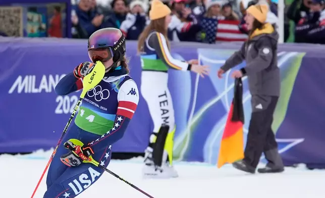 United State's Mikaela Shiffrin reacts as she looks back to see her disappointing time as Germany's Emma Aicher, background left, and Kira Weidle Winkelmann celebrate winning the silver medal in an alpine ski, women's team combined race, at the 2026 Winter Olympics, in Cortina d'Ampezzo, Italy, Tuesday, Feb. 10, 2026. (AP Photo/Robert F. Bukaty)