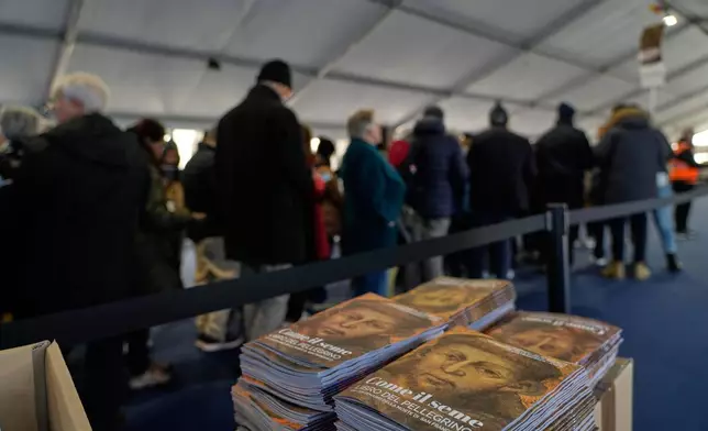 Pilgrims pass through security checks as they queue to honor the bones of St. Francis during the first public display inside the St. Francis Basilica, marking the 800th anniversary of the saint's death, in Assisi, Italy, Sunday, Feb. 22, 2026. The booklet with an image is St. Francis reads: "Like the seed, booklet of the pilgrim". (AP Photo/Gregorio Borgia)