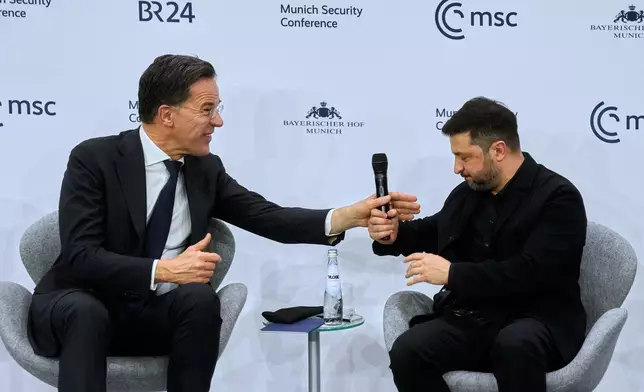 NATO Secretary General Mark Rutte, left, hands Ukraine's President Volodymyr Zelenskyy a microphone during a panel discussion at the Munich Security Conference in Munich, Germany, Saturday, Feb. 14, 2026. (AP Photo/Michael Probst)