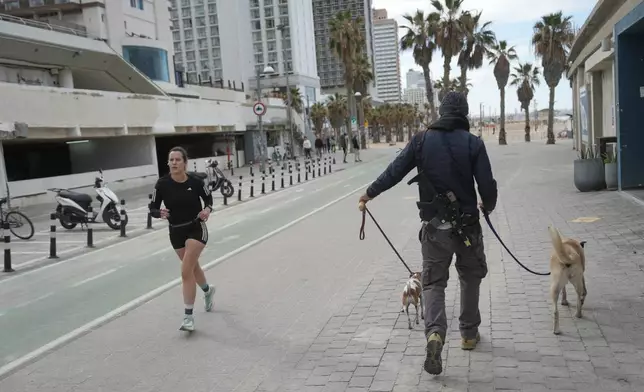 An armed man walks his dogs while a woman jugs after alarms announced that Israel had launched an attack on Iran, in Tel Aviv, Israel ,Saturday, Feb. 28, 2026. (AP Photo/Oded Balilty)