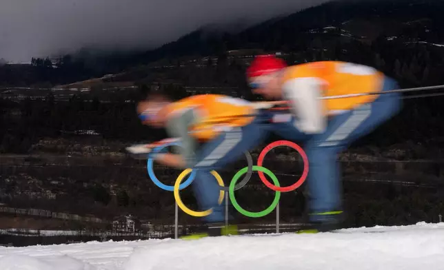 Athletes ski past Olympic rings during a cross country training session at the 2026 Winter Olympics, in Tesero, Italy, Thursday, Feb. 5, 2026. (AP Photo/Evgeniy Maloletka)
