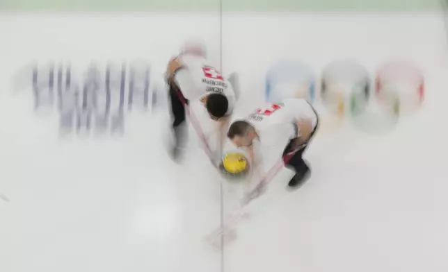 Switzerland's Pablo Lachat-Couchepin and Sven Michel sweep ahead of the stone during a men's curling round robin match against the United States at the 2026 Winter Olympics, in Cortina d'Ampezzo, Italy, Thursday, Feb. 12, 2026. (AP Photo/David J. Phillip)