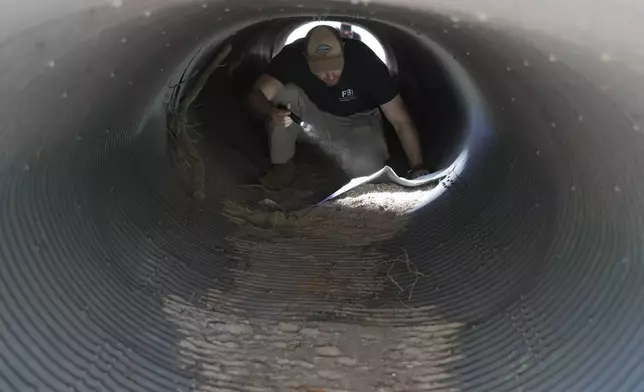 An investigator looks inside a culvert in the neighborhood where Annie Guthrie, whose mother Nancy Guthrie has been missing for more than a week, lives just outside Tucson, Ariz., on Tuesday, Feb. 10, 2026. (AP Photo/Ty ONeil)
