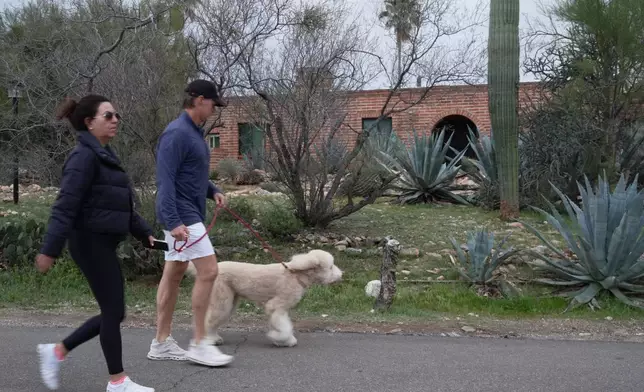 People walk by Nancy Guthrie’s home in the early morning under cloudy skies on Friday, Feb. 13, 2026 in Tucson, Ariz. (AP Photo/Ty ONeil)